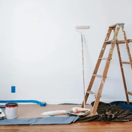 A room prepared for renovation with a ladder, paint supplies, and drop cloth.